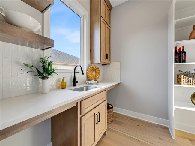 A window overlooks the outdoors from this functional scullery featuring light hardwood flooring.