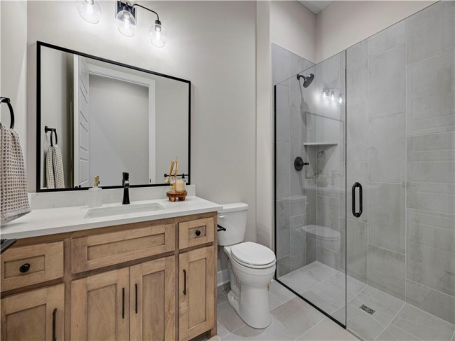 Tiled walk-in shower complements a warm wood vanity in this sleek bathroom.