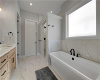 A freestanding tub sits beneath a large window in this master bath with marble-patterned tile flooring.