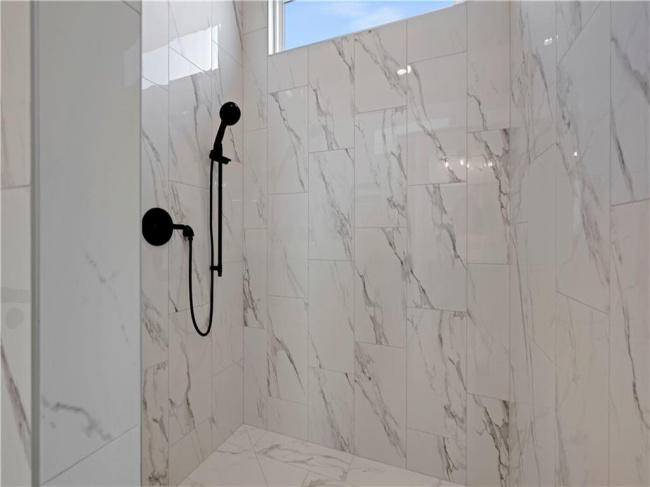 Elegant marble-patterned tile lines this modern shower featuring sleek matte black hardware.