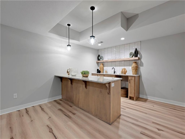 Gleaming stone countertops and warm wood flooring define this stylish custom wet bar area.