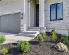 A welcoming concrete entryway accented by stone details is framed by neat landscaping.