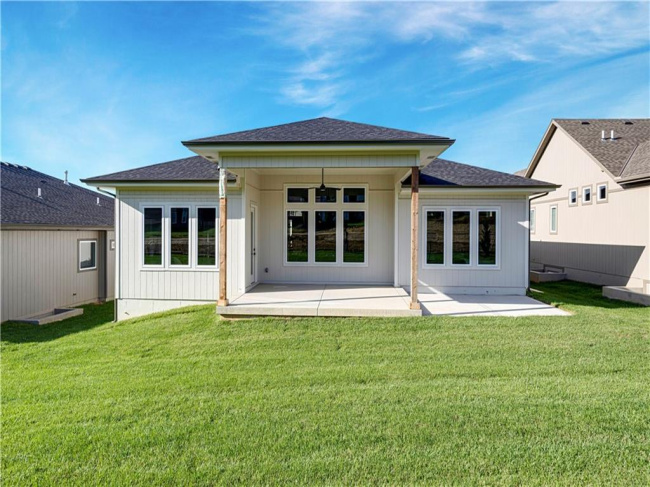 A spacious covered patio overlooks a lush green lawn under clear blue skies.