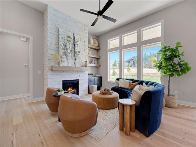 Sunlight streams through towering windows into a welcoming living space anchored by a stone fireplace.
